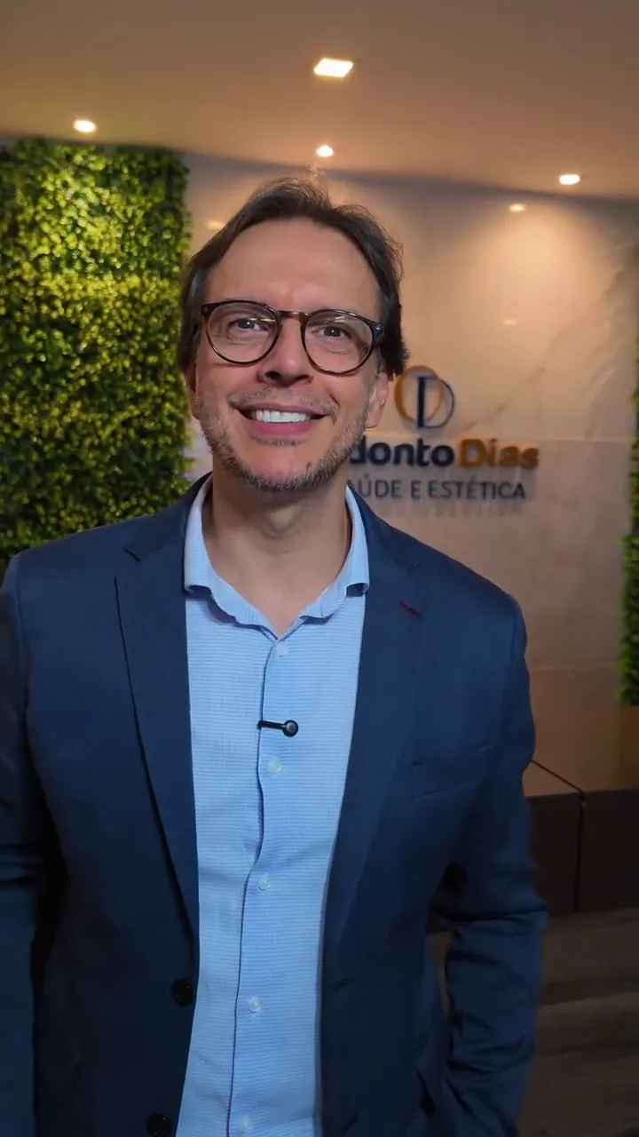 Dr. Valdemar sorrindo na recepção da clínica, com a logo ao fundo
